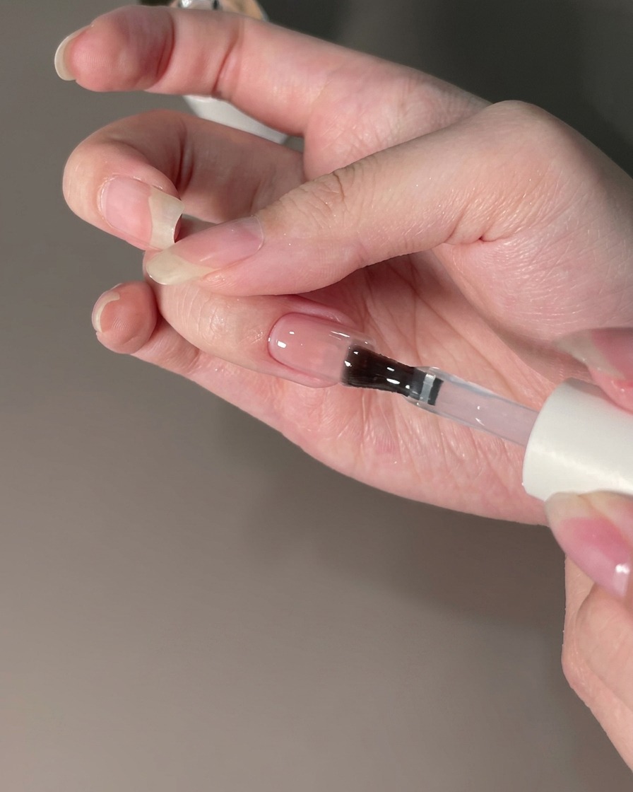 Ein Pinsel trägt einen Top-Coat-Versiegeler über einen mit Chrompuder veredelten Nagel auf.