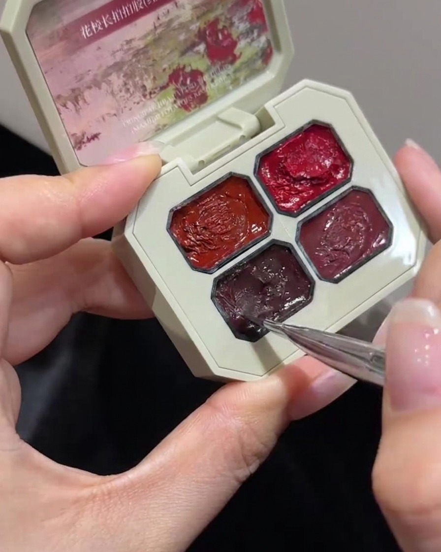 Nahaufnahme eines feinen Nageldesign-Pinsels, der leicht in ein bestimmtes Fach einer mehrfächerigen rosafarbenen Gel-Palette eintaucht.