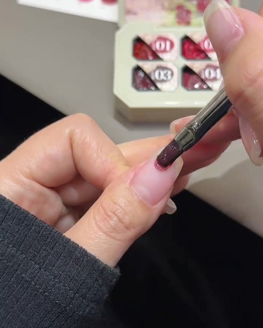 Ein Nagelpinsel tupft roséfarbenes Gel auf die Spitze eines Naturnagels.