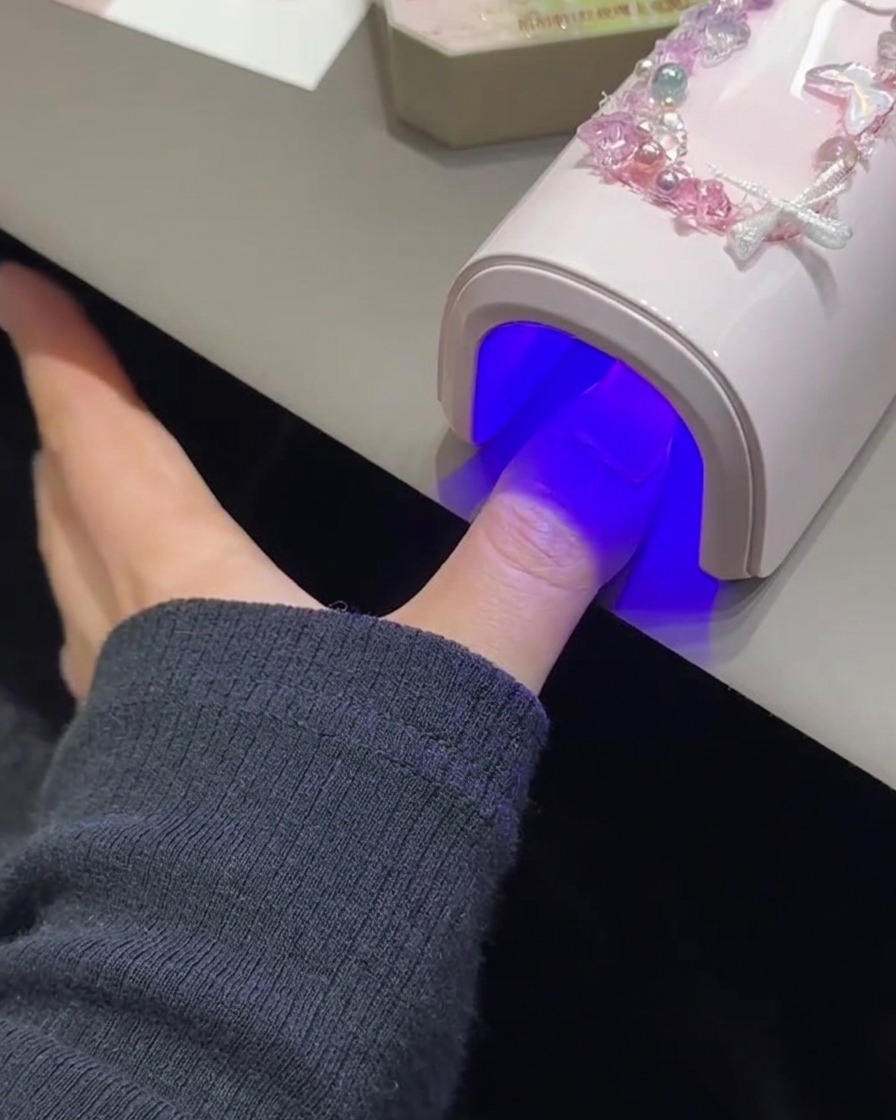 Ein Fingernagel beim Aushärten unter einer pinkfarbenen UV- und LED-Lampe.