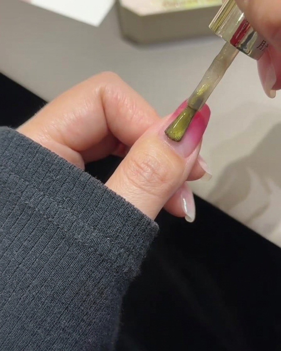 Ein Pinsel trägt goldenes Cat-Eye-Gel über einem ausgehärteten Rosé-Gradienten-Nagel auf.