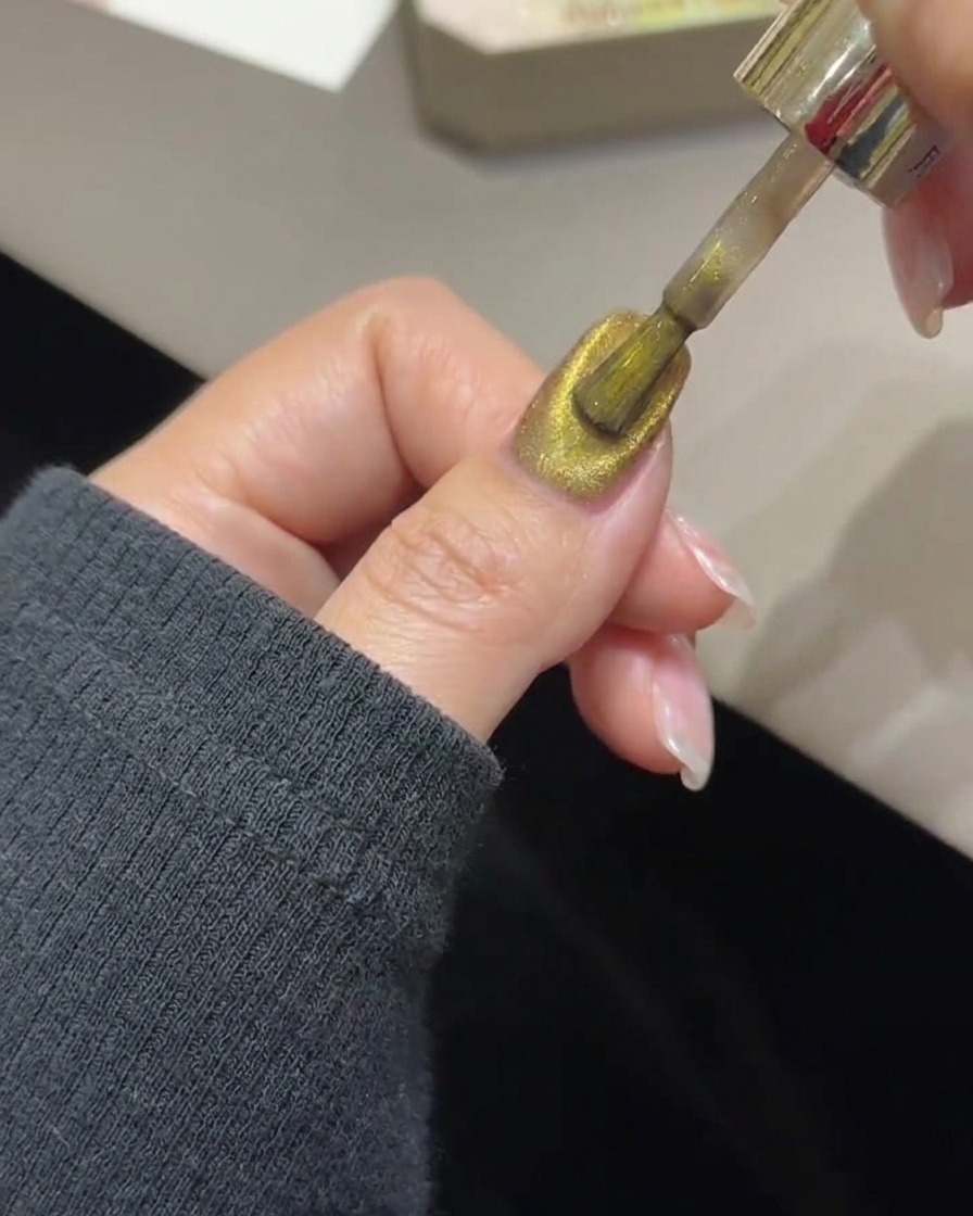 Ein magnetisches Stabwerkzeug schwebt über einem Nagel, um goldene magnetische Partikel zu einem Lichtband zu konzentrieren.