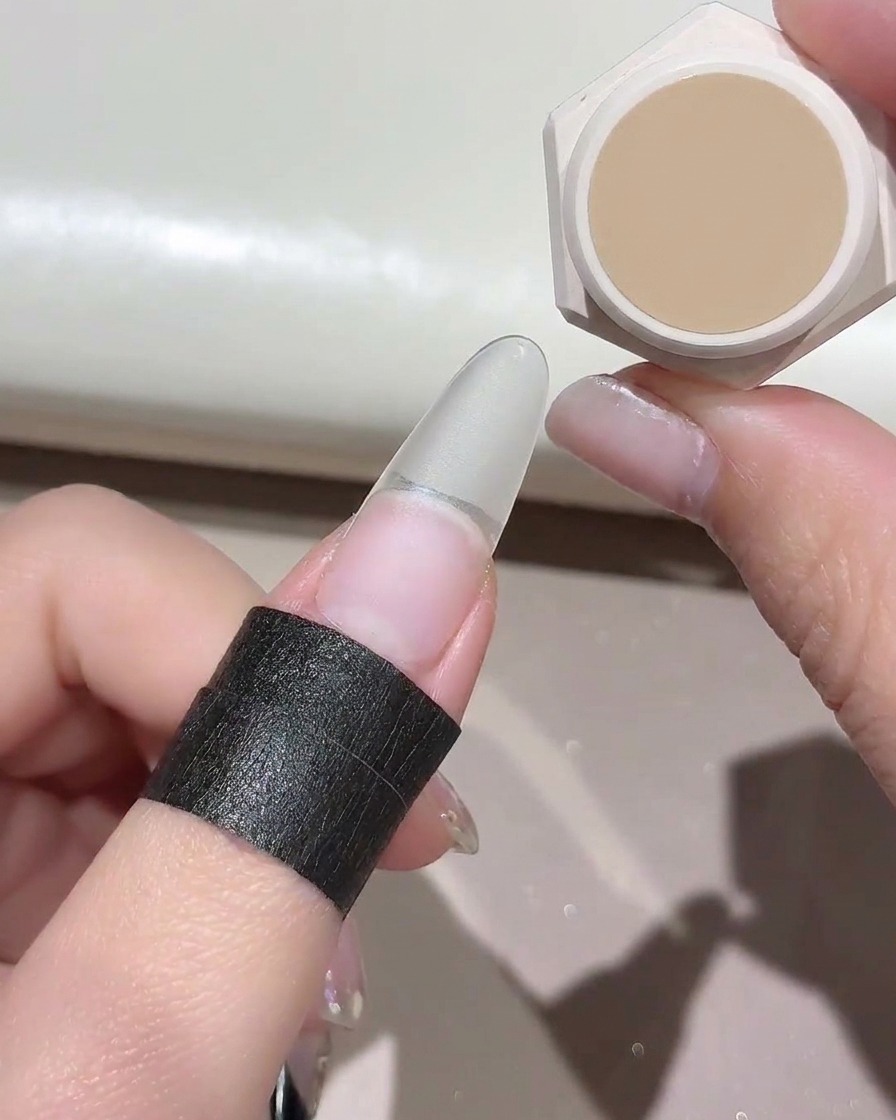 Ein kleiner Schwamm tupft eine Nude-Gelfarbe auf einen klaren Kunstnagel.