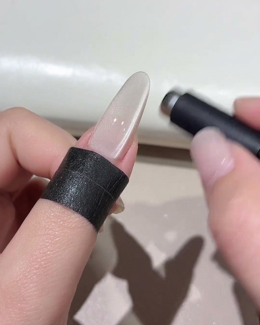 Ein zylindrischer Magnet schwebt über einem schimmernden Cat-Eye-Nagel, um den Lichteffekt zu formen.