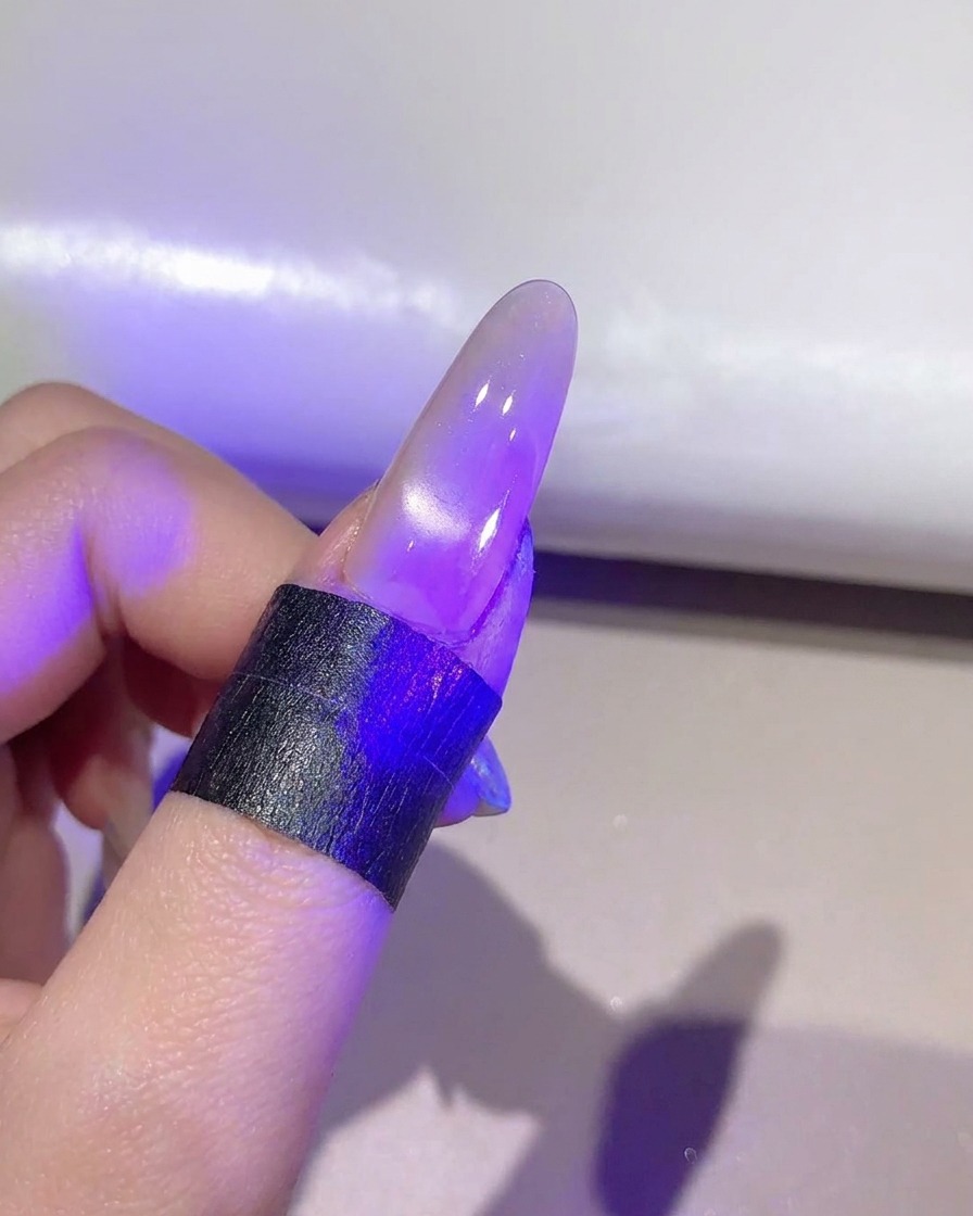 Ein Nagel härtet unter einer violetten UV/LED-Lampe die fertige Cat-Eye-Gelschicht aus.