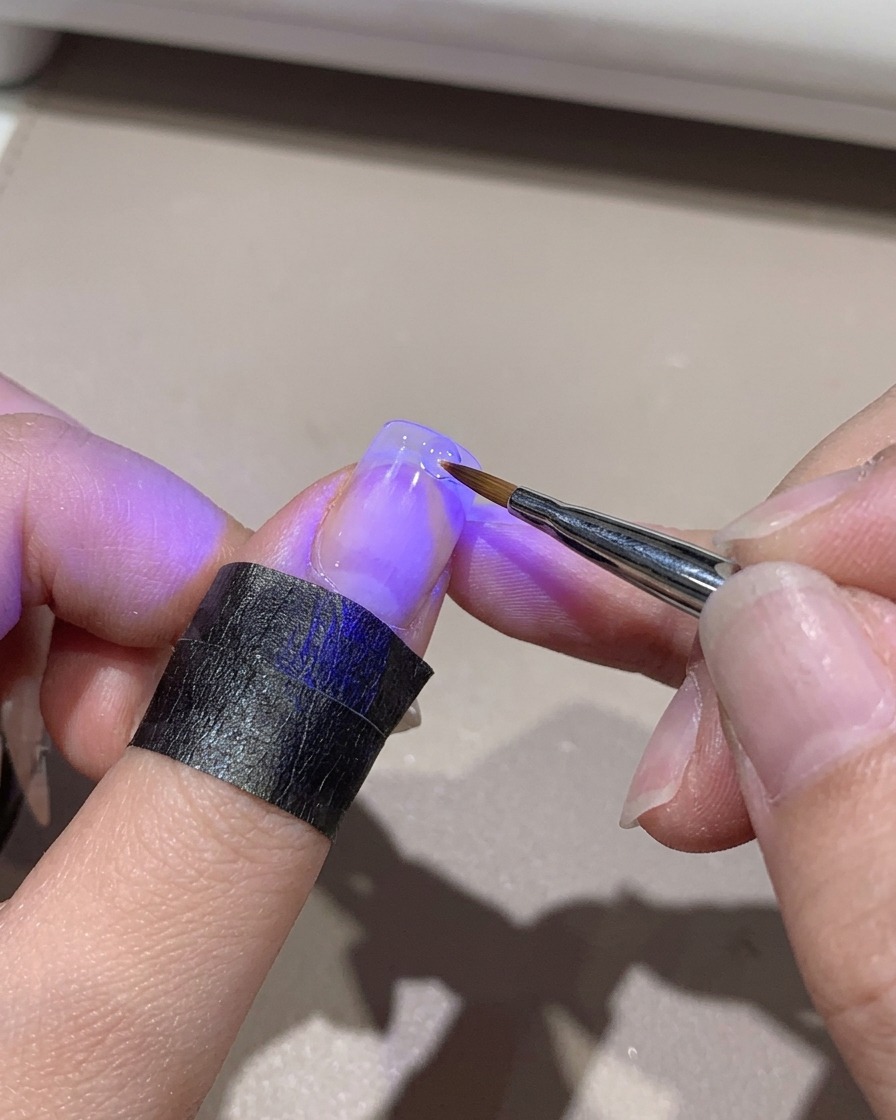 Eine Mini-UV-Lampe härtet eine Verlauf-Nagelspitze aus, die per Hand gehalten wird.