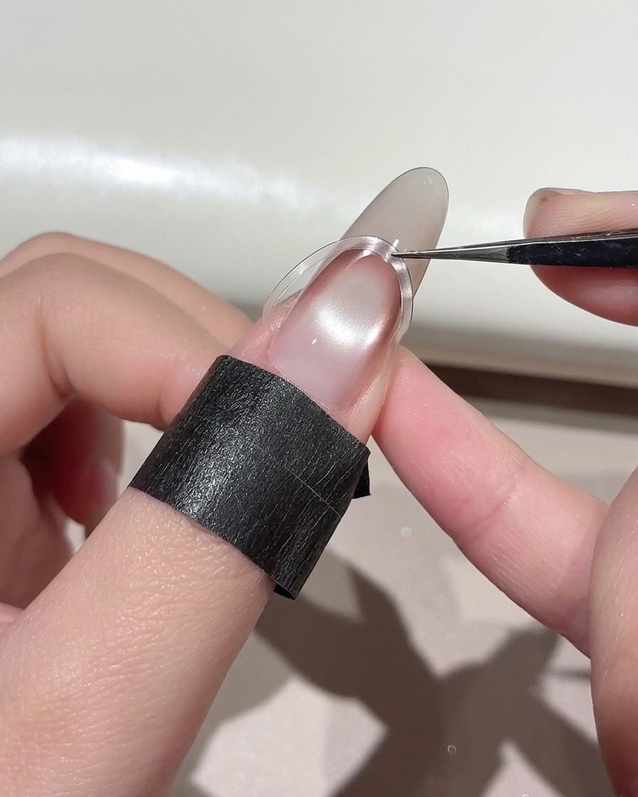 Eine Pinzette platziert einen gebogenen French-Nagelsticker etwas höher auf einem manikürten Nagel.