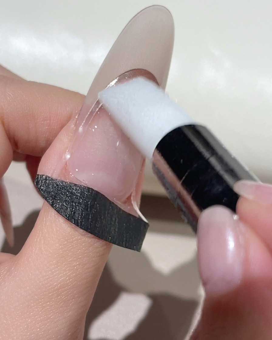 Ein weißes Silikon-Make-up-Tool drückt eine gebogene French-Schablone auf einen naturfarbenen Nagel.