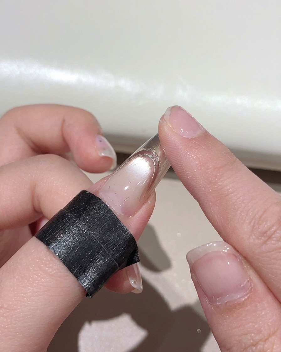 Ein Finger reibt metallisches Roségold-Puder auf die Spitze eines manikürten Nagels.
