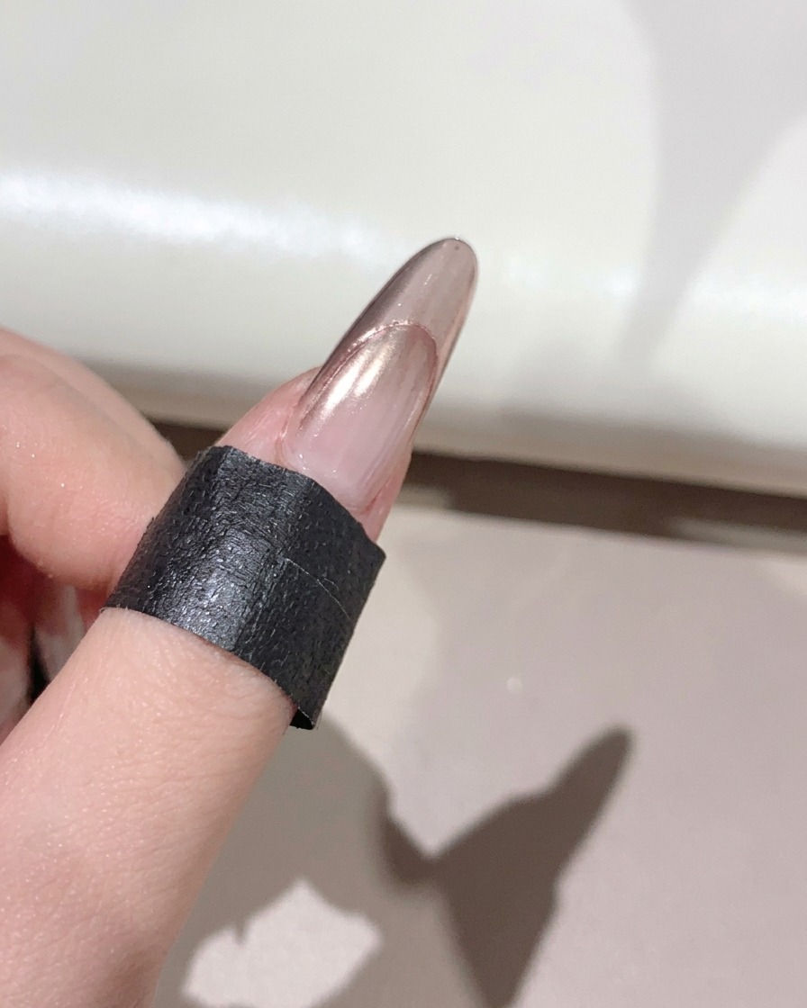Ein flauschiger Pinsel streicht überschüssiges Puder von einem glänzenden, manikürten Nagel.