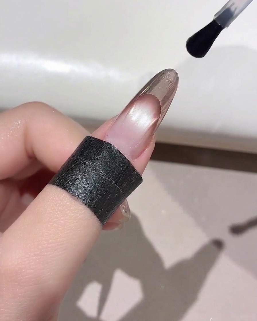 Ein Nagelpinsel trägt klaren Top Coat über die Spitze einer fertigen French Manicure auf.