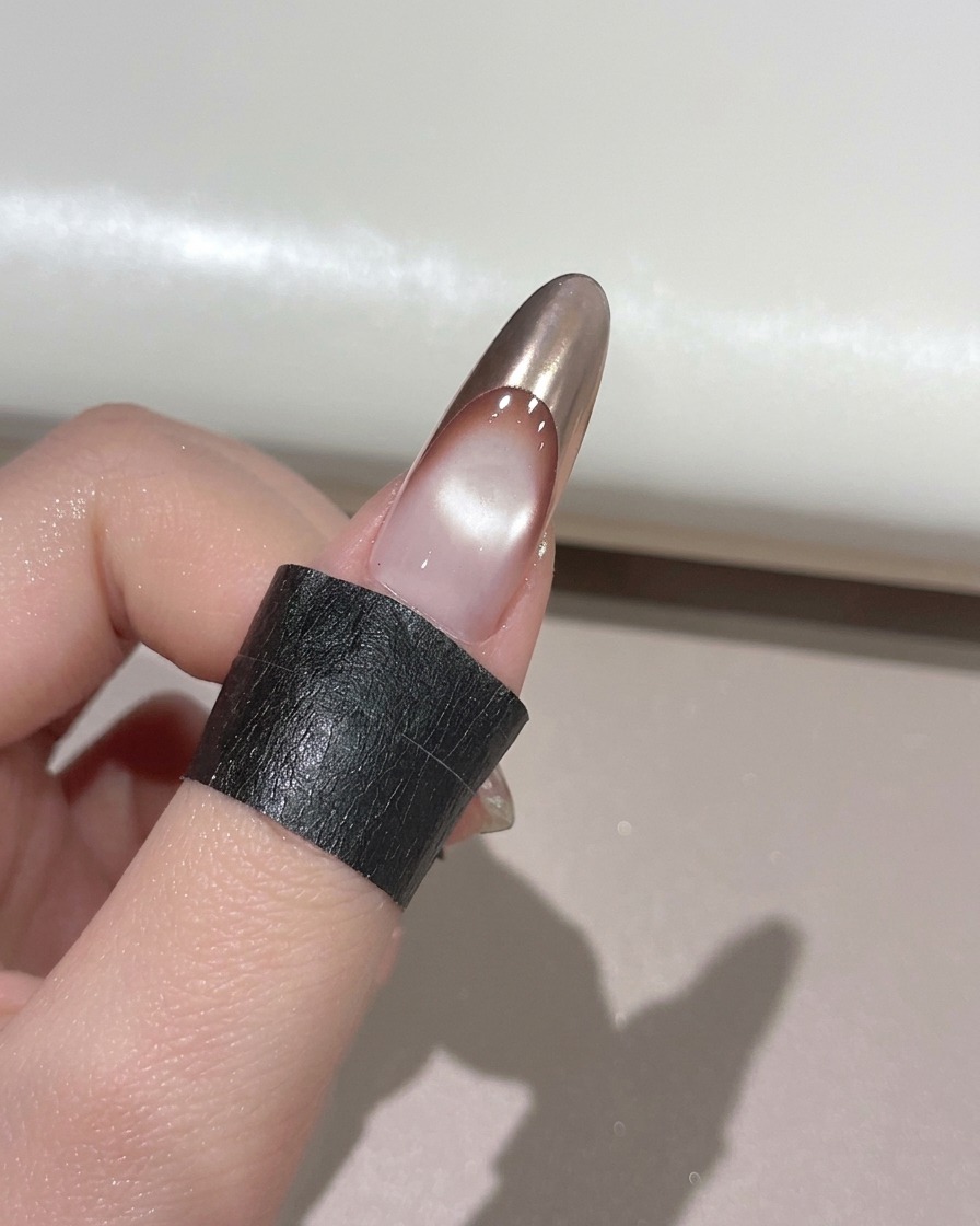 Ein Finger mit einer goldenen Chrome-French-Spitze ruht zum Aushärten in einer UV-Nagellampe.