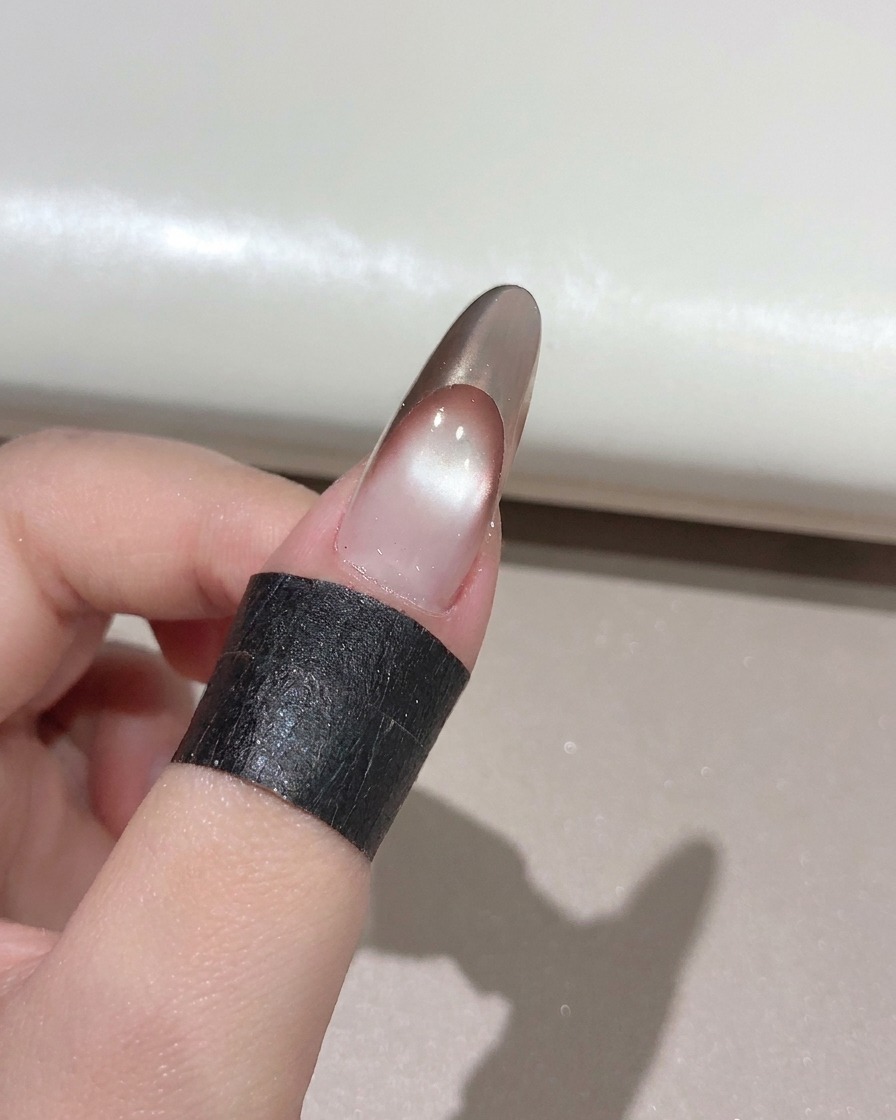 Ein Nagelpinsel trägt einen klaren, glänzenden Top Coat über eine fertige French Manicure in Roségold auf.