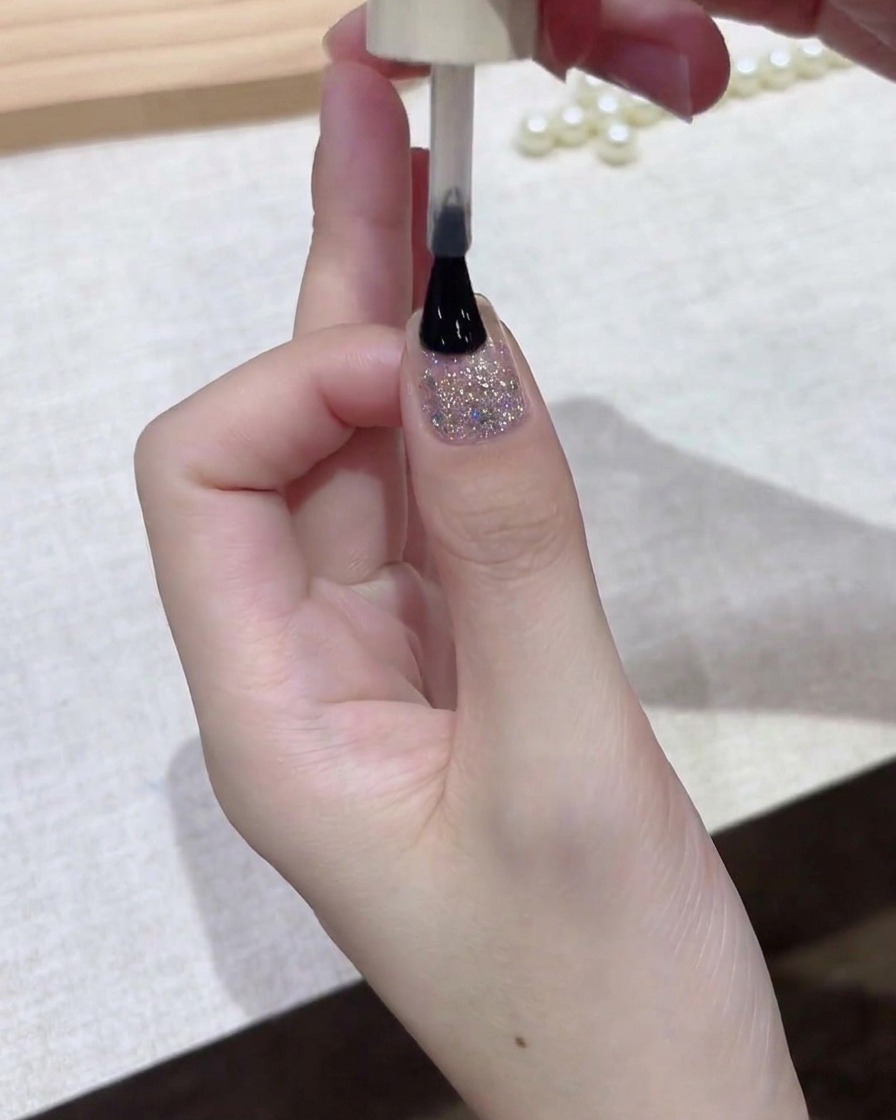 Ein Pinsel trägt eine dünne Schicht dunklen Gel-Nagellacks über die Nageloberfläche auf.