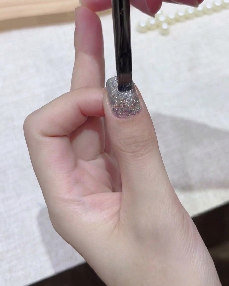 Ein feiner Pinsel glättet eine dunkle Gelschicht gleichmäßig über die Nagelplatte.