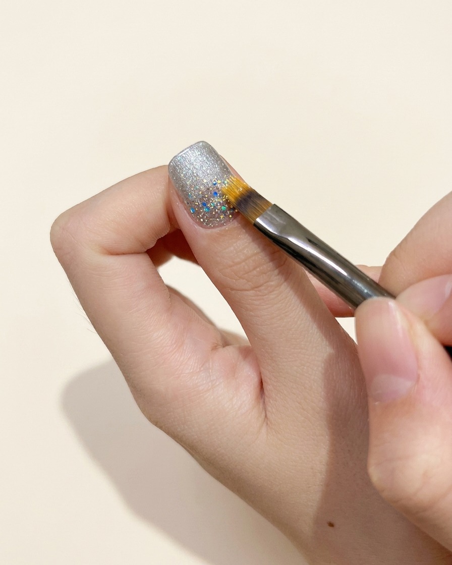 Ein Korrekturpinsel verfeinert die Ränder eines Gel-Auftrags in der Nähe der Nagelhaut eines Fingernals.