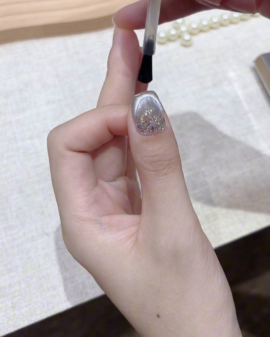 Ein Pinsel trägt einen klaren, glänzenden Topcoat über einen fertigen silbernen magnetischen Gelnagel auf.