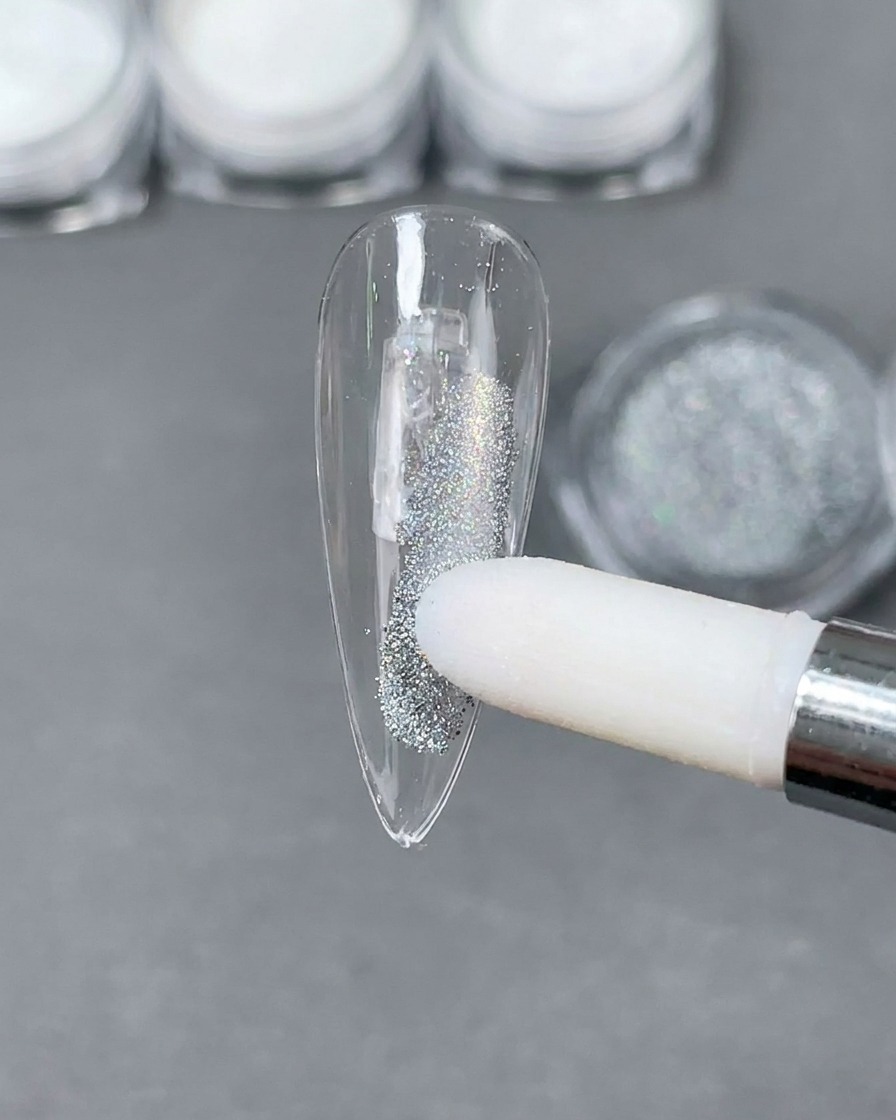Ein Schwammapplikator platziert silbernes Laser-Holografie-Pulver auf eine klare Stiletto-Nagelspitze.