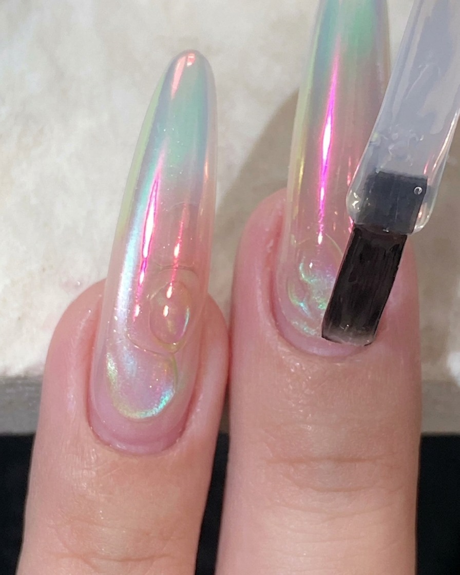 Ein flacher Nagelpinsel trägt einen klaren, glänzenden Top-Coat auf einen langen Nagel auf.