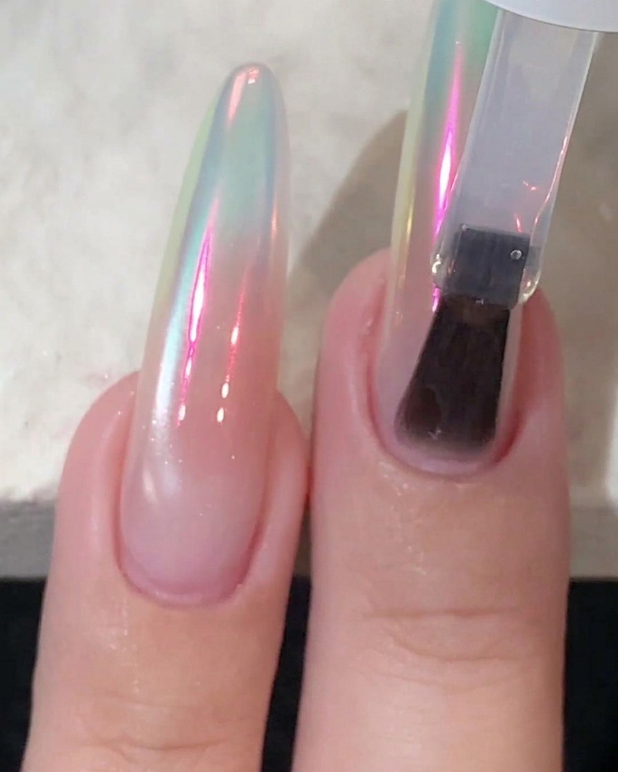 Ein Schwamm-Applikator poliert Chrom-Puder auf einen glänzenden Nagel, bis er einen Aurora-Glanz reflektiert.