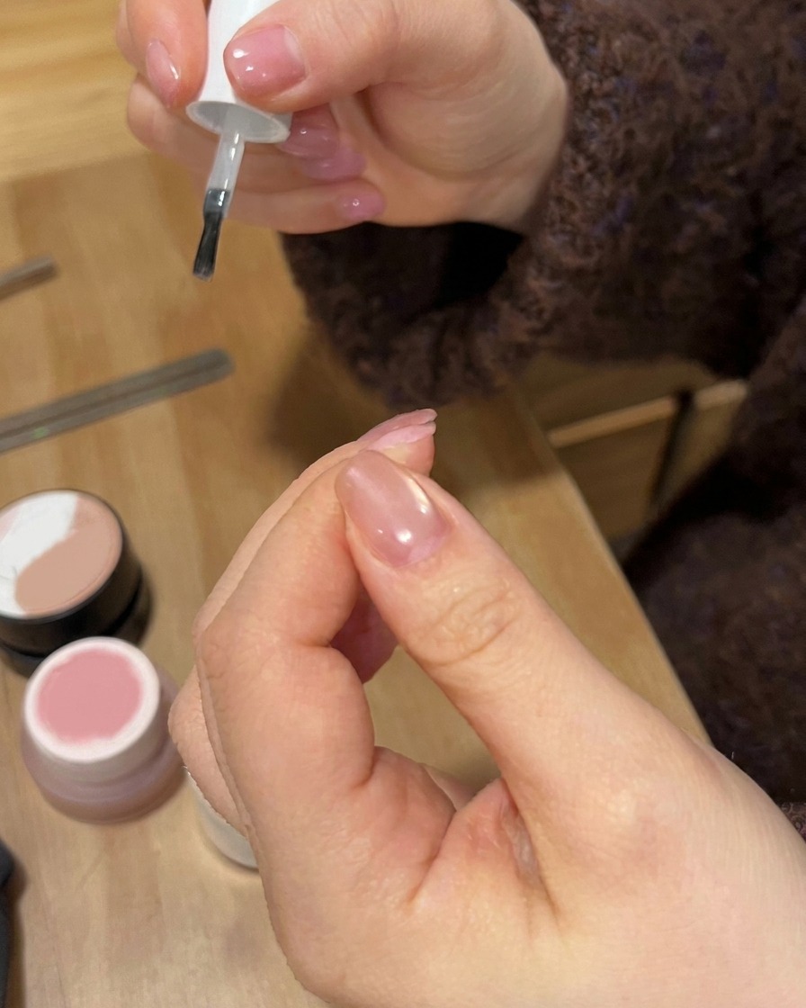 Ein Nagellackpinsel trägt eine glänzende Klarlackschicht über ein fertiges Gradient-Nageldesign auf.