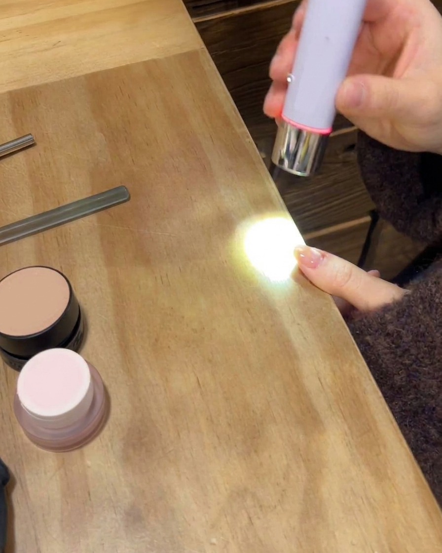 Eine tragbare UV/LED-Lampe härtet den finalen Glossy-Topcoat auf einer manikürten Hand aus.
