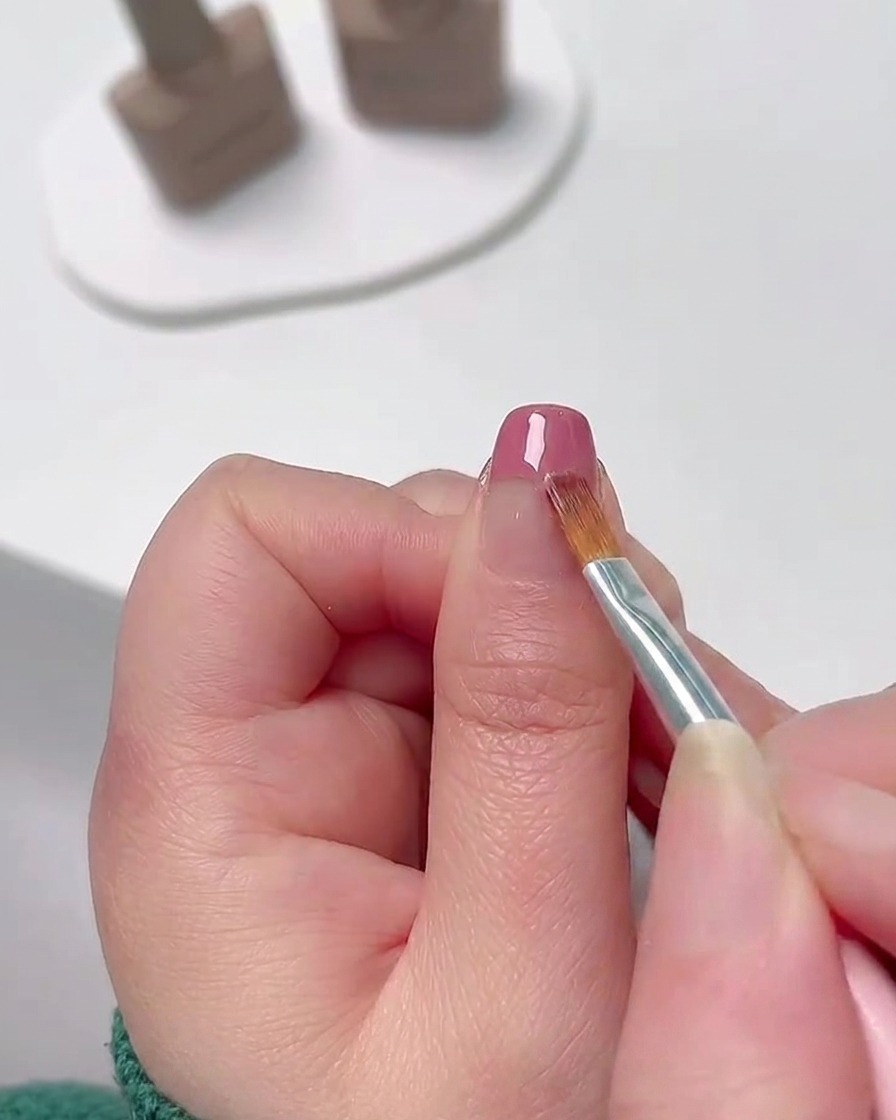 Eine Nahaufnahme eines feinen Nail-Art-Pinsels, der rosa Gel-Nagellack von der Nagelspitze nach unten verblendet, um einen sanften Farbverlauf zu erzeugen.