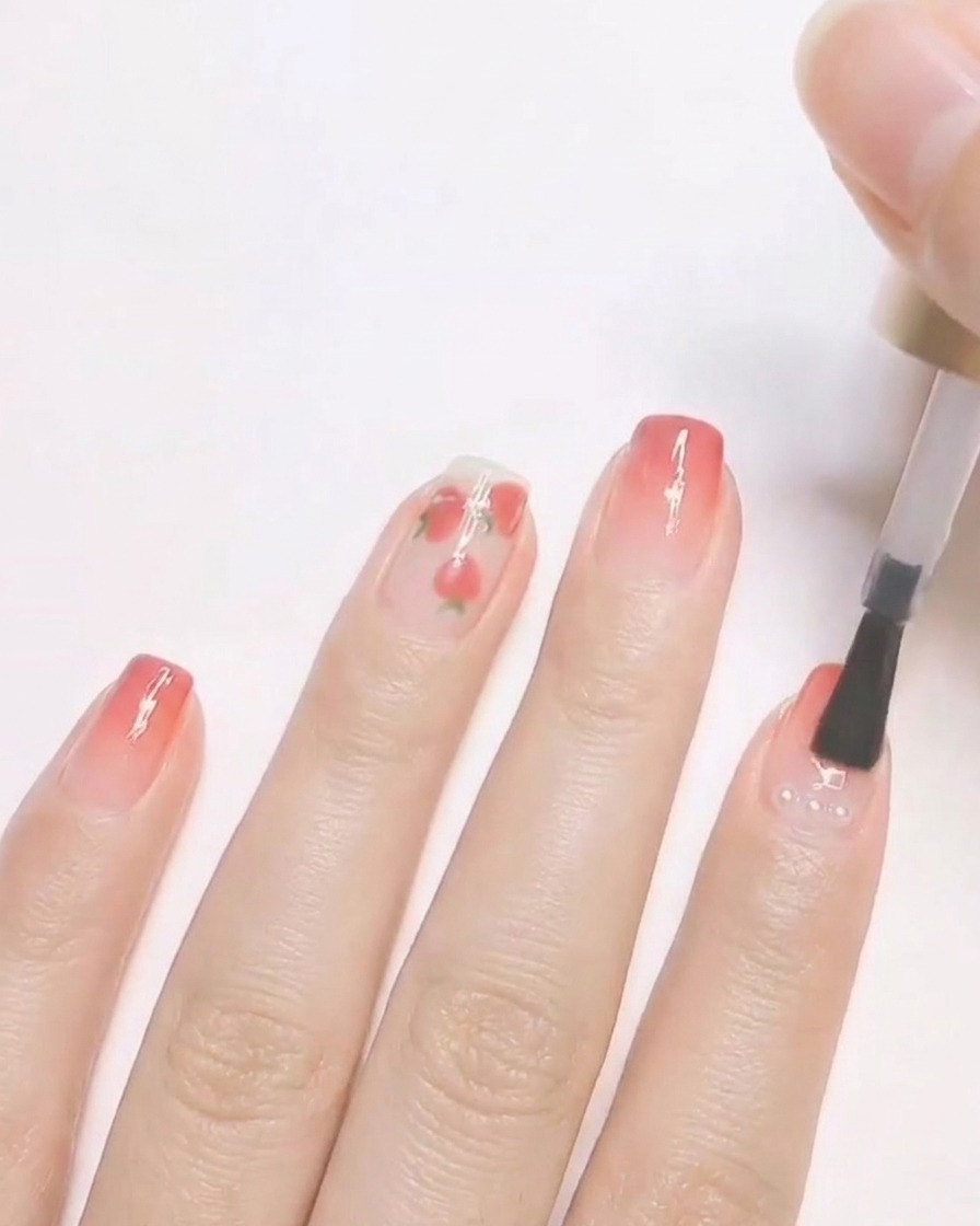 Ein Nagelpinsel trägt klaren Topcoat über einem fertigen Nageldesign mit kleinen eingekapselten Perlen auf.