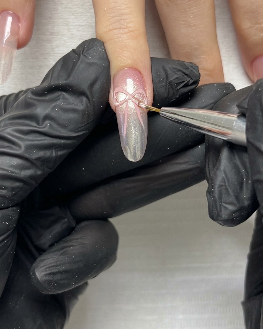 Eine Nahaufnahme eines feinen Pinsels, der die zarten Ränder und Enden einer rosa 3D-Schleife auf einem manikürten Nagel verfeinert.
