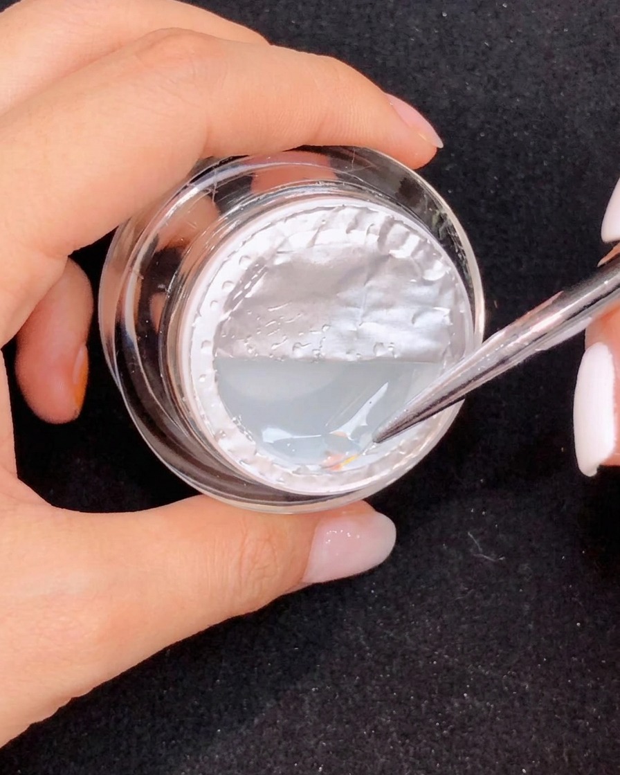 Ein feiner Pinsel zieht eine lange Tränenform aus klarem Gel auf einem pinkfarbenen Ombre-Nagel.
