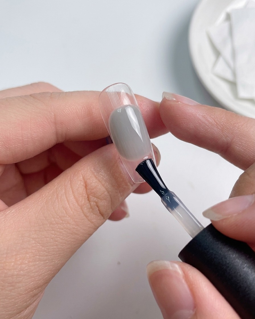 Ein Pinsel trägt eine Schicht Top Coat über einem farbigen Nagel auf.