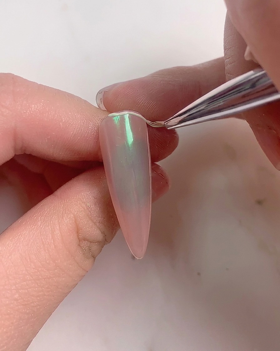 Ein weicher Pinsel wischt überschüssiges Puder von einem fertigen Aurora-Nagel ab.