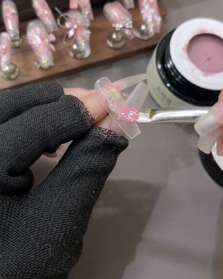 Ein flacher Gelpinsel verteilt halbtransparentes, milchig-rosa Gelpolish über einen Nagel mit Glitterflakes in der Mitte.