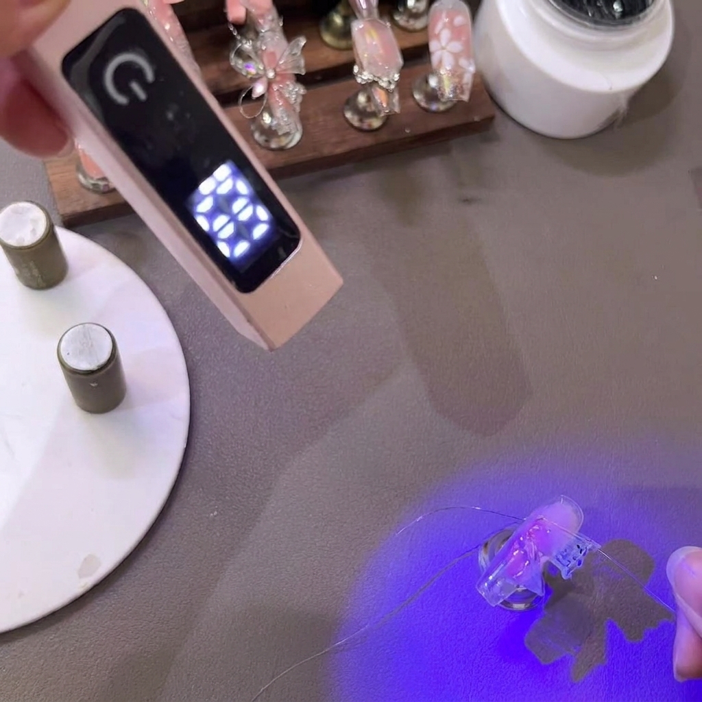 Eine Pinzette zieht und formt die zarten Spitzen eines PVC-Gel-Schmetterlingsflügels unter einer Mini-UV-Lampe.