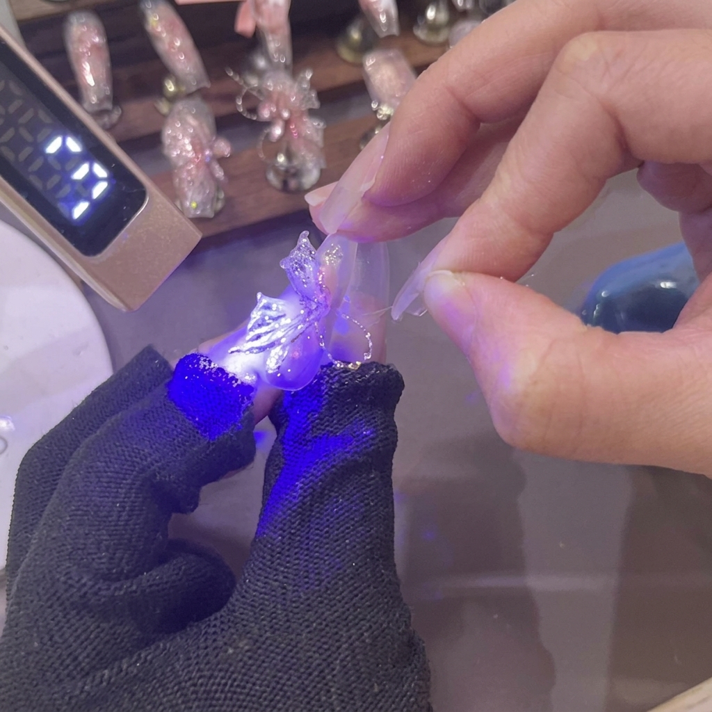Eine Mini-UV-Lampe strahlt violettes Licht auf einen frisch geformten 3D Rosa-Gel-Schmetterlingsflügel auf einem Fingernagel.