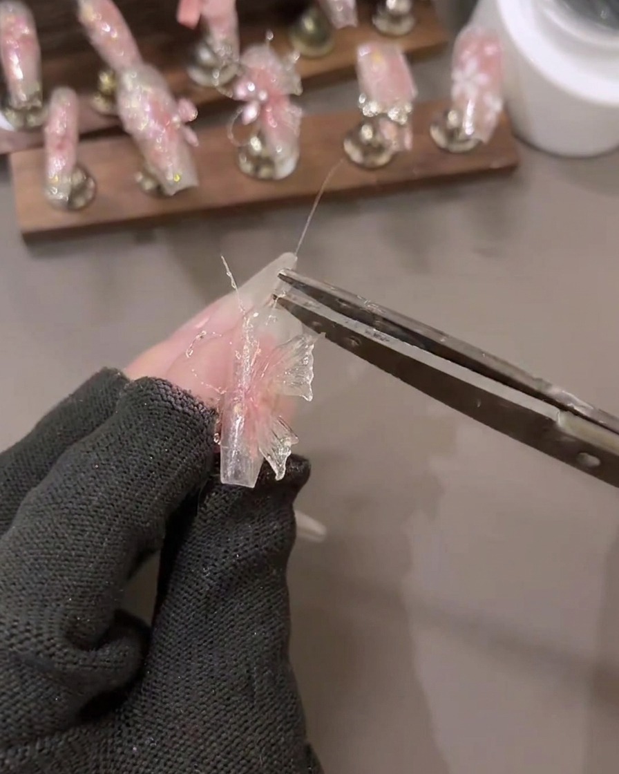 Nahaufnahme einer Hand, die Shattered Diamond Glitter Gel Details auf ein 3D-Nail-Art-Design mit bereitliegenden Werkzeugen aufträgt.