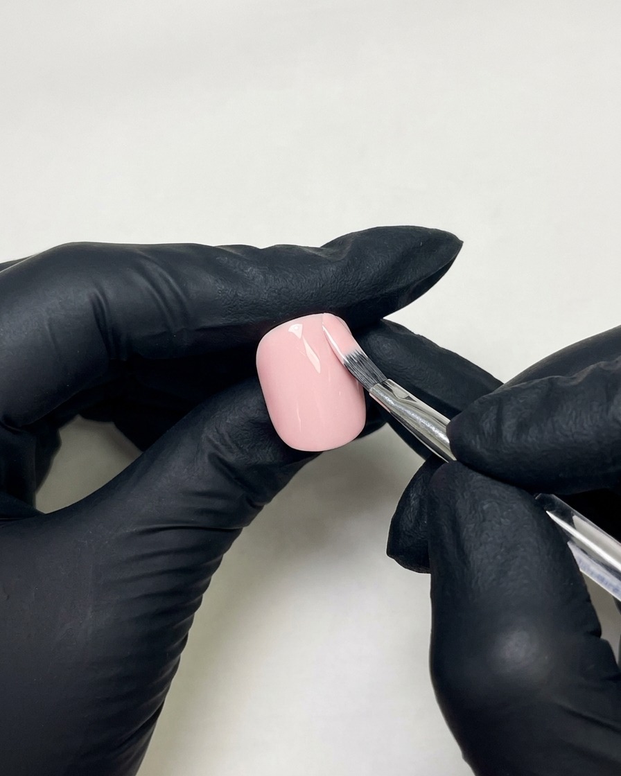 Beweumte Hände verwenden einen flachen Nagelpinsel, um hautfarbenen Rosa-Gel-Lack auf einen vorbereiteten Fingernagel aufzutragen.