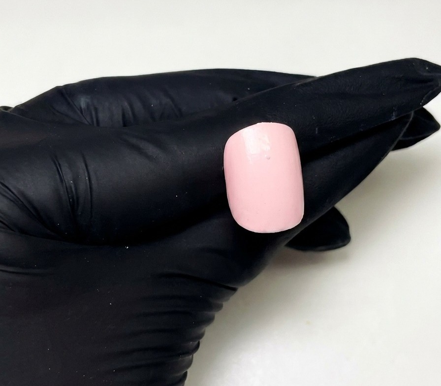 Eine Nahaufnahme eines vorbereiteten rosa Nagels mit einem einzelnen kleinen Punkt aus rosa Aufbau-Gel in der oberen Mitte.