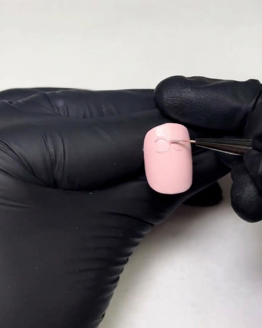 Beweumte Hände zeichnen die zweite Schlaufe einer 3D-Gel-Schleife mit einem feinen Liner-Pinsel auf einen Nagel.