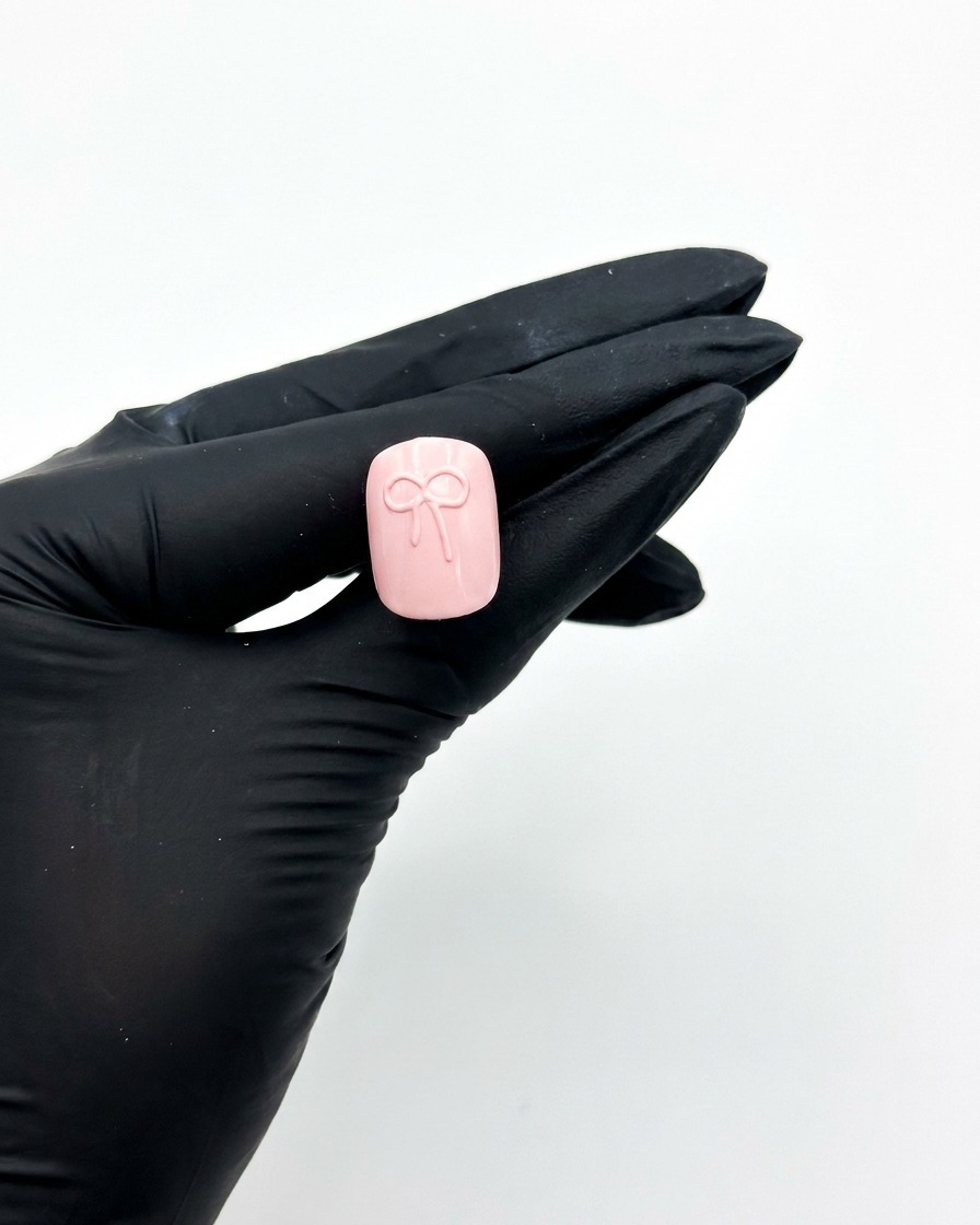 Eine be Handschuhe getragene Hand hält einen rosa Press-on-Nagel unter eine UV-Nagellampe, um das 3D-Schleifendesign auszuhärten.