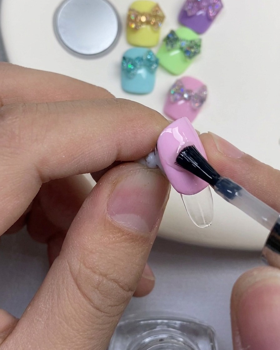Ein schwarzer Nagelpinsel trägt klares Verstärkungsgel auf einen rosa lackierten Nagel auf.