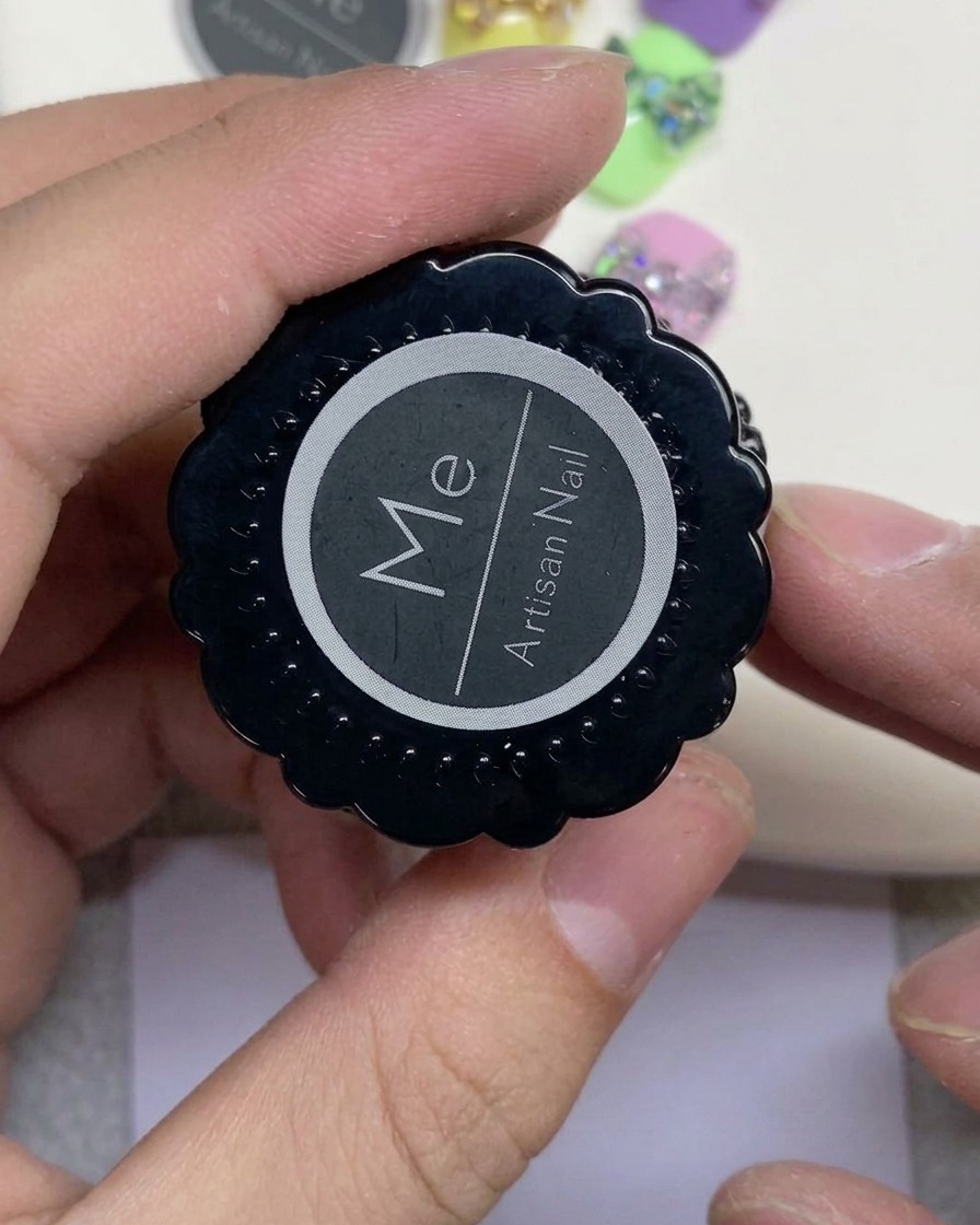 Eine Hand hält einen schwarzen Tiegel mit der Aufschrift Artisan Nail und einem weißen runden Logo.