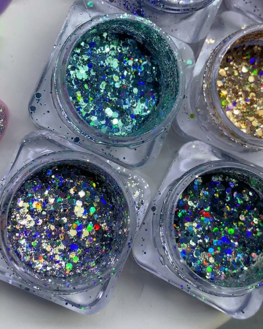Ansicht von oben auf mehrere kleine Tiegel, gefüllt mit bunten, holografischen und metallischen Glitzerflocken.
