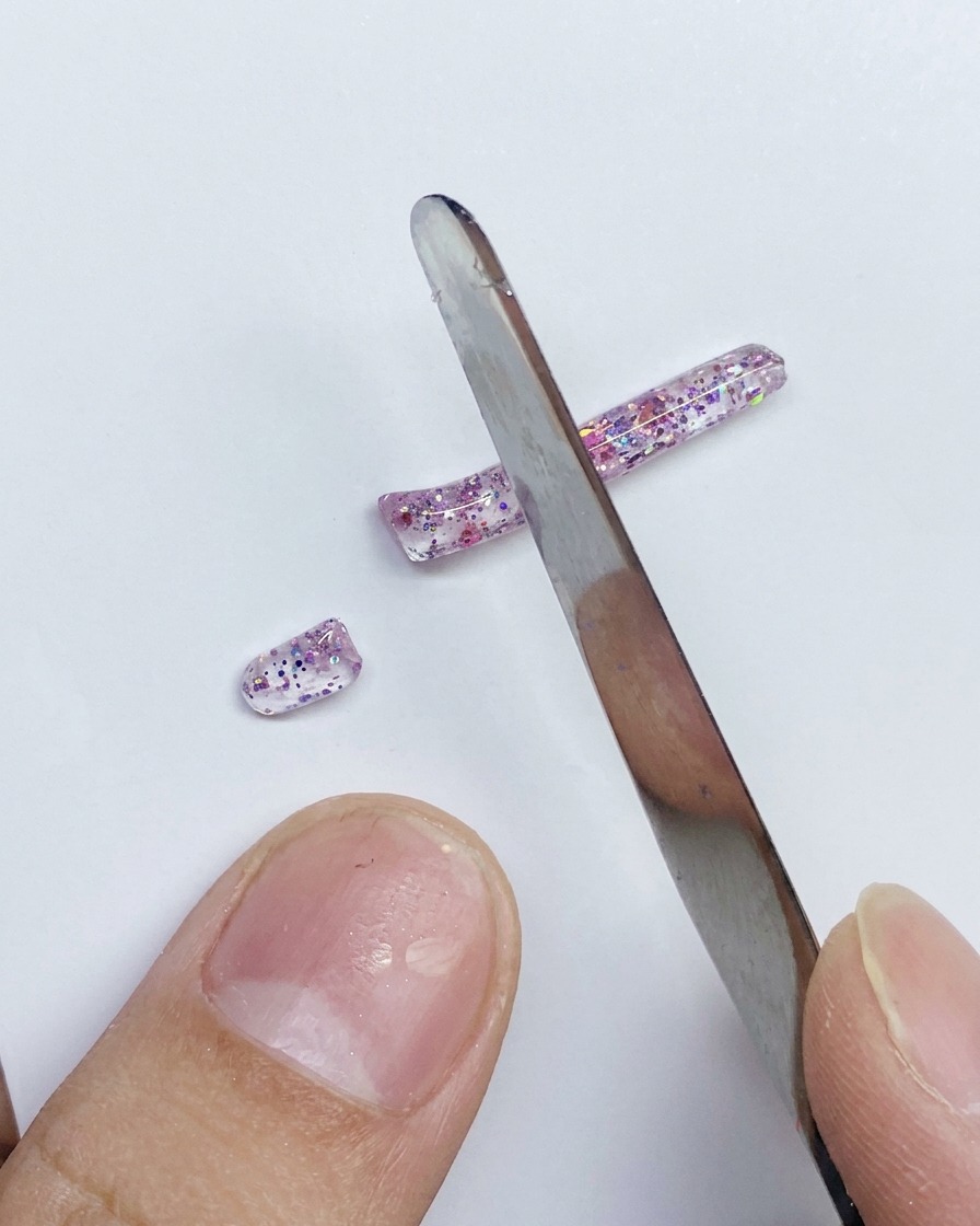 Ein Metallspatel schneidet einen langen Streifen aus rosa glitzerndem PVC-Gel in kleinere Segmente.