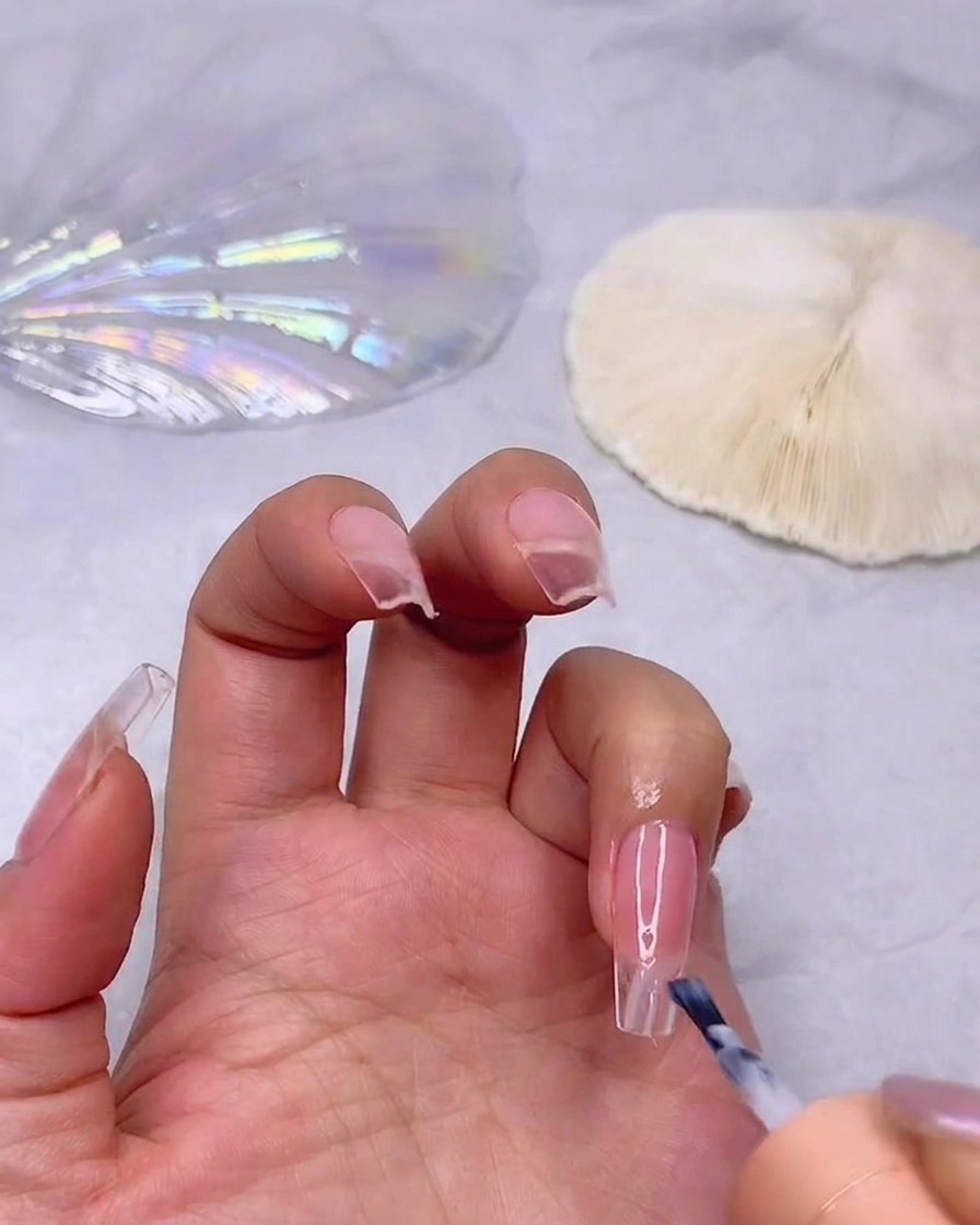 Ein Pinsel trägt eine Schicht milchig-weißen UV-Lack auf die Spitze eines rosafarbenen Nagels auf, um den Ombré-Effekt zu starten.