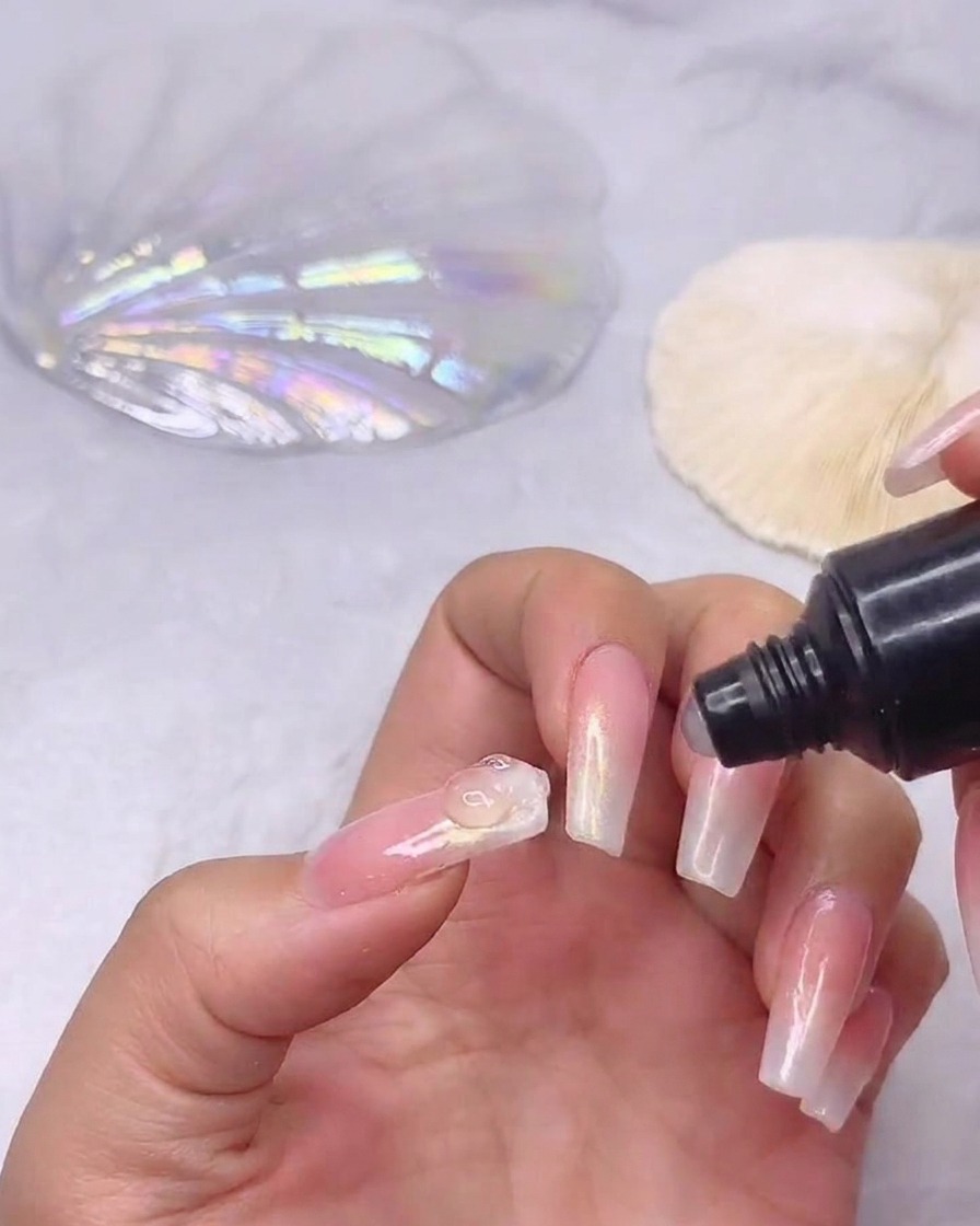 Eine Tube Strass-Klebegel gibt einen kleinen, klaren Tropfen Kleber in die Mitte eines vorbereiteten Ombré-Nagels.
