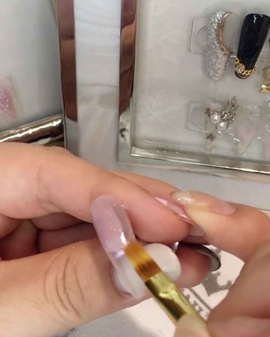 Ein flacher Nagelpinsel verblendet pinkes Gel in der Mitte der Nagelplatte nach unten.