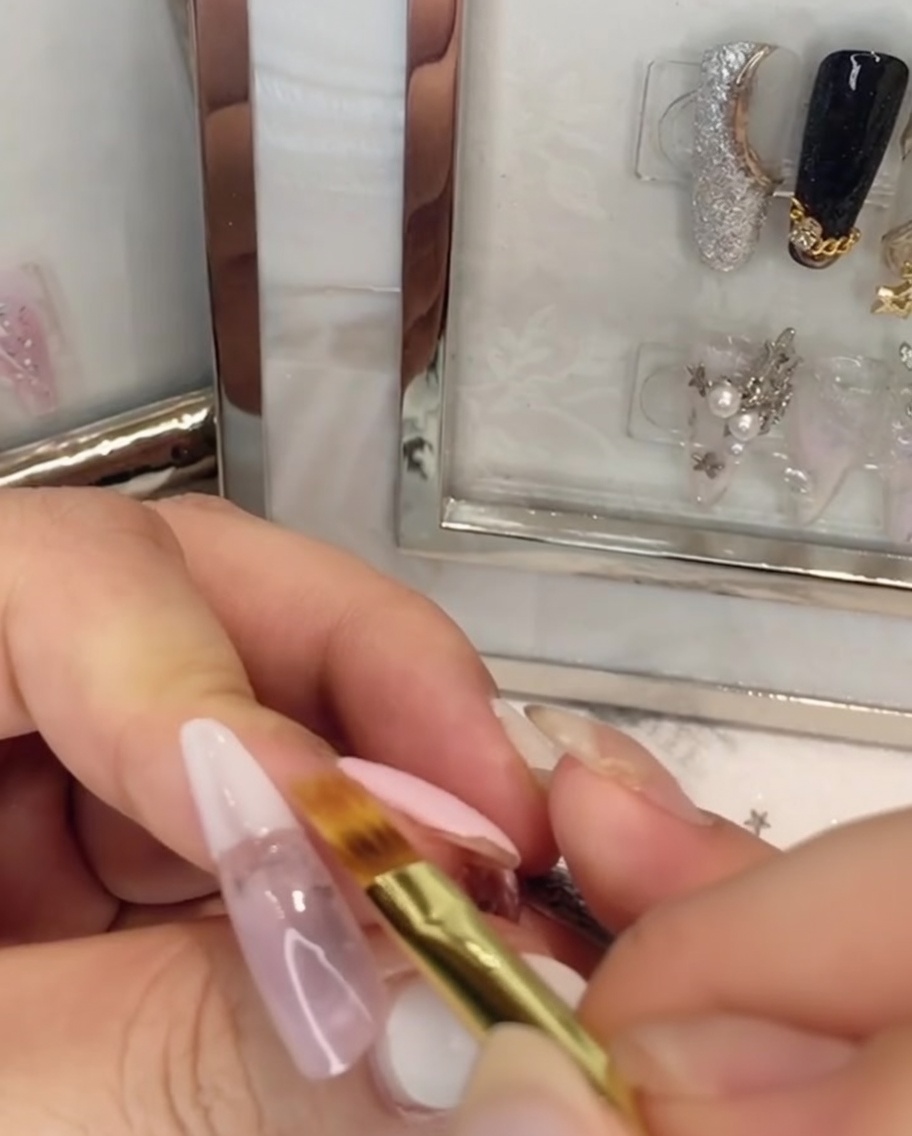 Ein flacher Pinsel verblendet weißen Gelack nach oben in das pinke Gel auf dem Nagel.