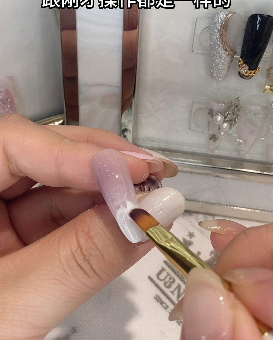 Ein Pinsel verblendet weißes Gel auf der unteren Hälfte eines Ombré-Nagels.