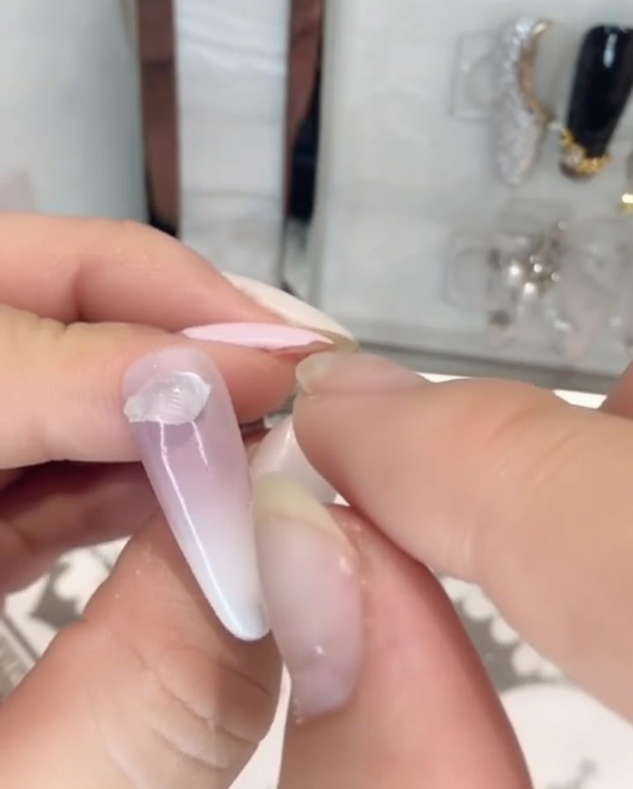 Finger platzieren ein Stück klaren, dicken festen Steinkleber auf den Nagelansatz eines lackierten Nagels.